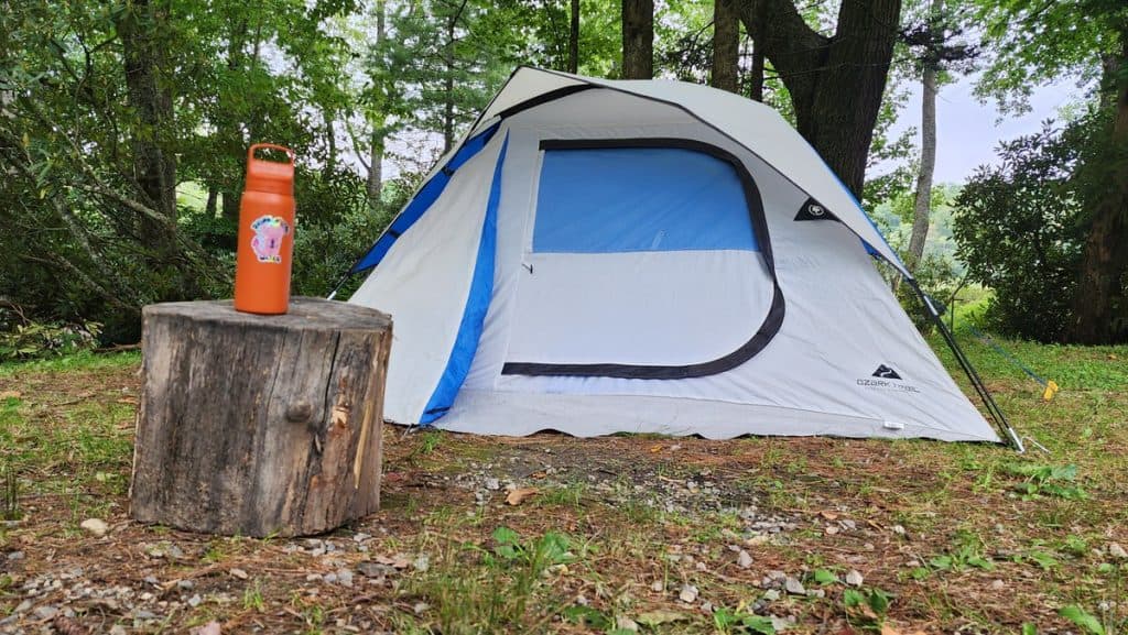 A LifeStraw Go filtered water bottle perched on top of a tree stump in front of our tent for camping in Blowing Rock, North Carolina. How does camping reduce stress?