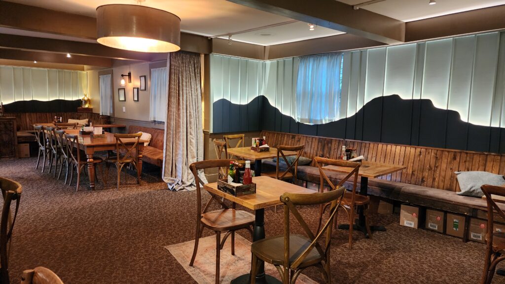 The cozy interior of the restaurant at Hellbender Bed and Beverage in Blowing Rock, featuring wooden tables and chairs, a cushioned bench along the wall, and soft lighting with mountain-shaped wall decor.