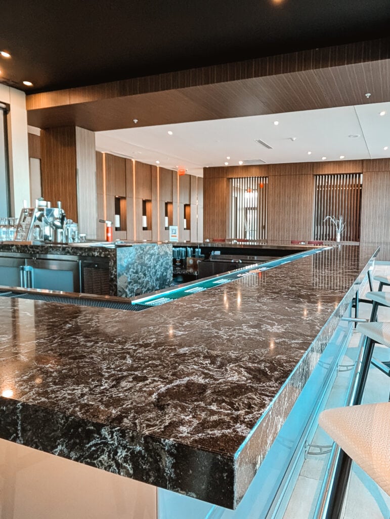 Contemporary bar at AC Hotel Downtown Huntsville with a marble countertop and wooden slatted wall panels, offering a minimalist and upscale atmosphere.