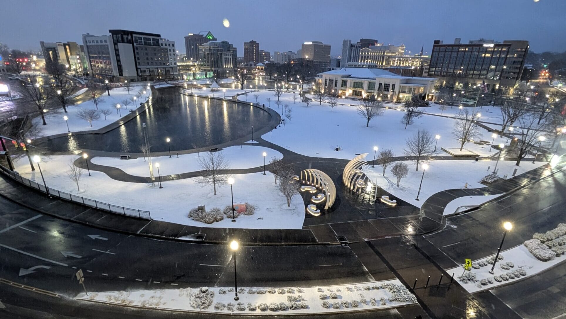 Snowy early morning view overlooking Big Spring International Park in Downtown Huntsville, Alabama, as seen from the accessible room at the AC Hotel. The park, roads, and nearby buildings are gently lit and blanketed in snow, creating a peaceful winter cityscape.