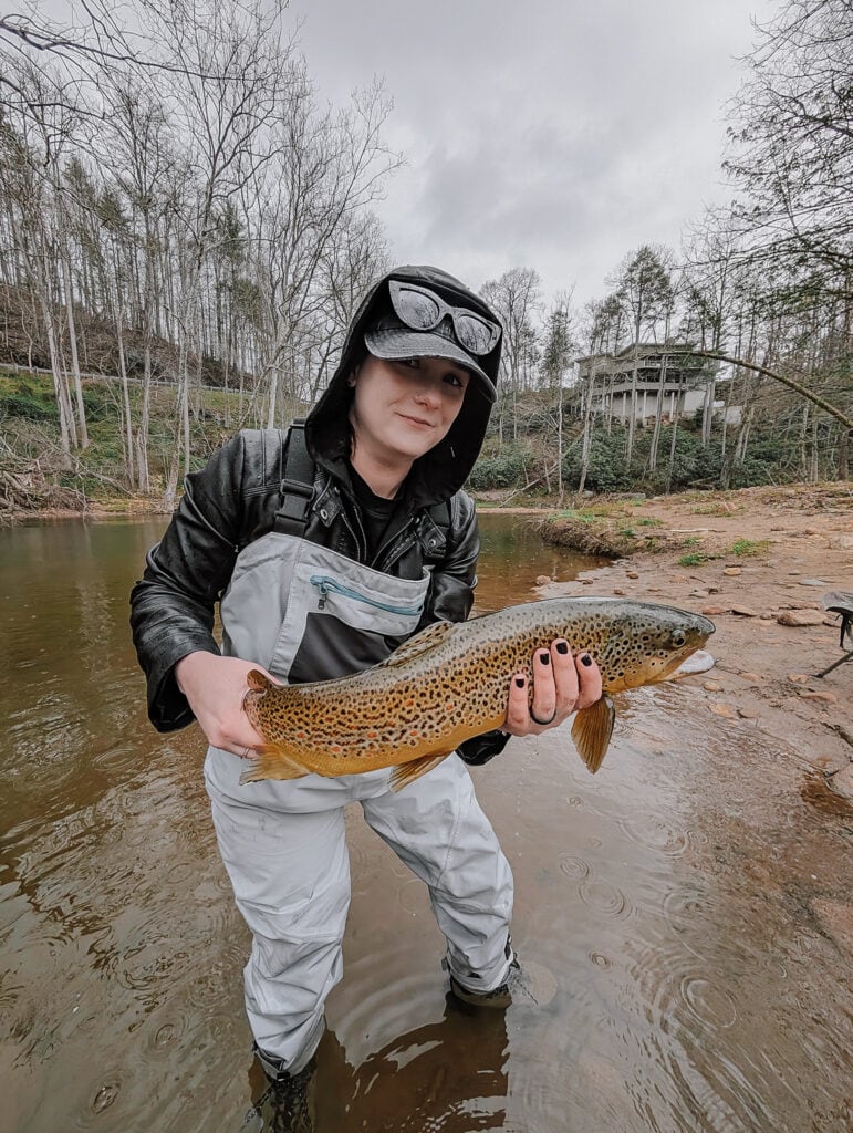 Phoenyx smiles while holding a large brown trout during a fly fishing experience with Chetola in Blowing Rock, NC.
