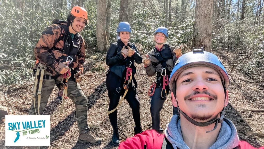 Group selfie at Sky Valley Zip Tours featuring four people in helmets and harnesses smiling and giving thumbs-up in the forest.