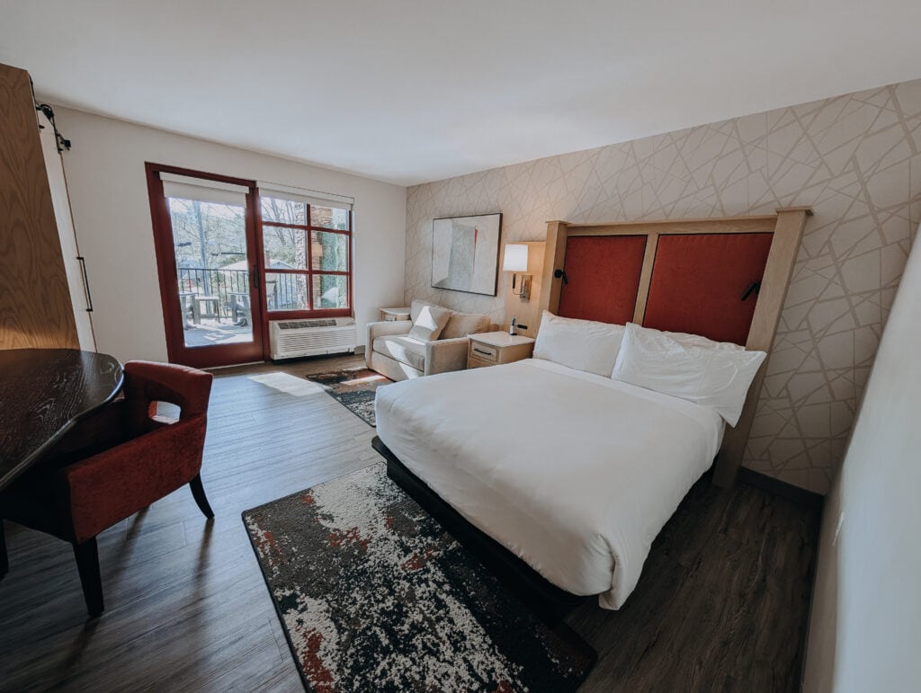 Bright accessible hotel room at The Embers featuring a queen bed, armchair, and door leading to a private balcony.