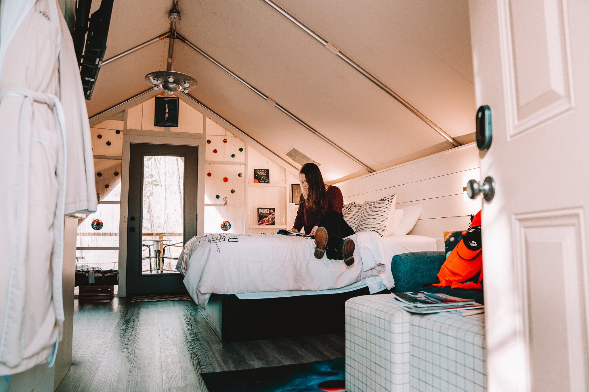 Woman relaxing on a bed inside a cozy, modern glamping tent at ReTreet Resort + Spa in Lake Guntersville, Alabama, with playful decor, a bright orange backpack, and forest views outside the glass doors. Featured image for the post Is Solo Travel Worth It on Phoenyx Travels. Featured image for 'How to Have a Rest Day That Actually Helps You Recover '.