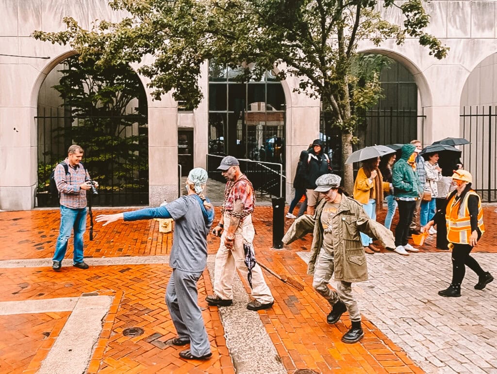 Costumed participants in bloody outfits carry props, including a severed head, during a Salem Halloween zombie parade. Featured image for the post 'What Salem Mass in October Is Really Like...'.