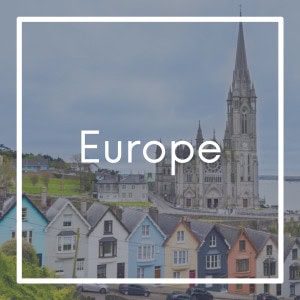 Square graphic labeled “Europe” with a backdrop of a picturesque European village. The image features pastel-colored row houses on a hill and a towering Gothic cathedral with a spire under a cloudy sky.