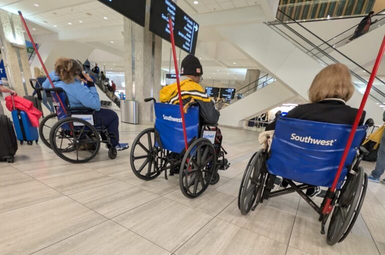 View from a wheelchair following three passengers in Southwest airport wheelchairs through Tampa International Airport with overhead signs reading “Rental Cars,” “Economy,” and “Public Bus.”