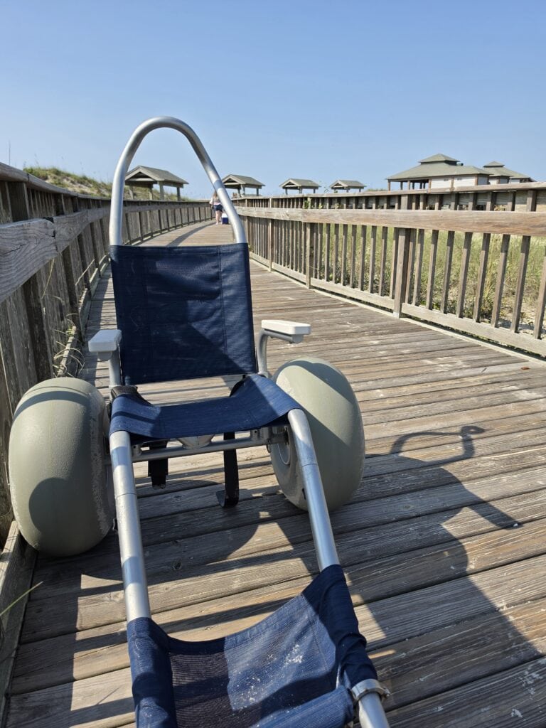 An adaptive beach wheelchair with oversized flotation wheels on an accessible coastal boardwalk on Bear Island in North Carolina.