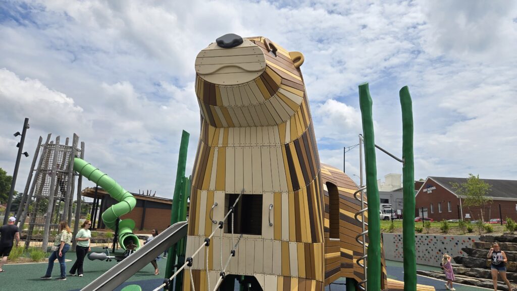 A giant otter shaped playground structure towers over the play area at Riverfront Park in Danville VA. Children and adults gather around the oversized brown and tan otter which includes climbing features slides and nearby play equipment making the park a family friendly option for things to do in Danville VA.